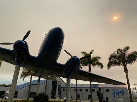 LOS ANGELES, CA, SEP 2021: Douglas DC3 Monument silhouetted with palm trees outside Museum of Flying at Santa Monica Municipal Airport, hazy afternoon with low, weak sun