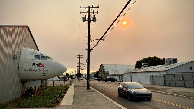 LOS ANGELES, CA, SEP 2021: side view, cockpit of jet aircraft used by FedEx appears to come through hangar wall to street with passing car at Museum of Flying, Santa Monica. Hazy sun visible