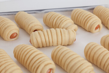 An uncooked sausage bread roll or hotdog bun rising on a baking tray preparing to put in oven. A bread made of a mix of flour, milk, water, sugar, salt, active dry yeast, and butter