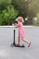 Child riding scooter. Little girl spending time outdoors in summer. Kid in a park.