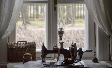 Retro-still life: Antique items - sewing machine, lamp, casket are on the window