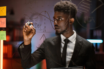 Close up blurred portrait of young handsome African American man, writing on glass board and making...