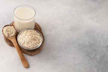 Glass cup of oat milk on a wooden board with an ingredient in a bowl on a light background top view