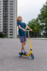 Child riding scooter. Smiling boy spending time outside in summer. Kid having fun near an apartment...