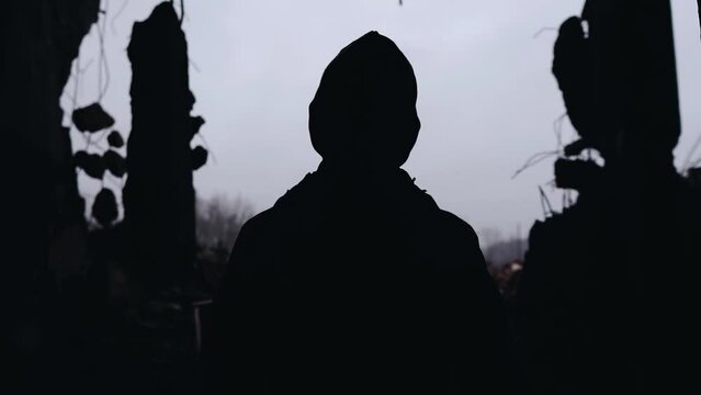 The guy is standing in the span of a broken bombed house. The camera captures his silhouette from behind. Shooting in motion
