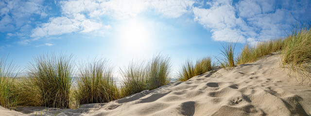 Panoramic landscape background banner panorama of sand dune, beach and ocean North Sea with blue sky, clouds and sunbeams