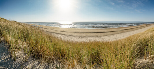 Panoramic landscape background banner panorama of sand dune, beach and ocean North Sea with blue sky, clouds and sunbeams