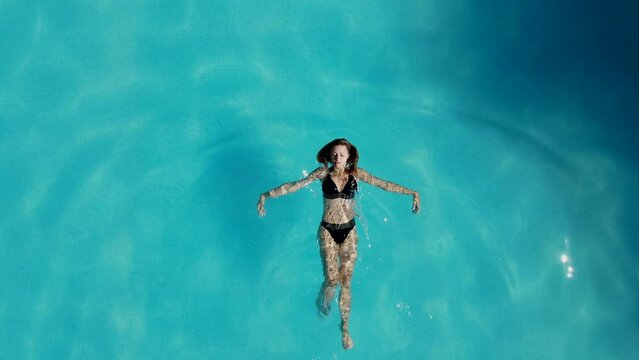 Beautiful girl in a swimsuit swims on his back in the pool top view. Taken from a drone