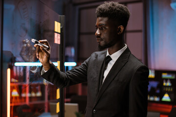 Focused african american male manager writing on glass board in modern office, planning start up...