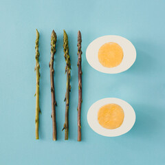 Wild asparagus and hard boiled egg arranged on light blue background. Seasonal healthy food minimal concept.