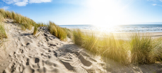 Panoramic landscape background banner panorama of sand dune, beach and ocean North Sea with blue sky, clouds and sunbeams