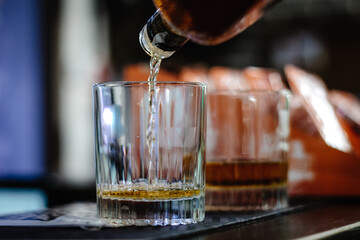 pouring whiskey, brandy, cognac or scotch from a bottle into a glass. strong alcoholic drink