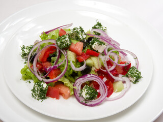 Vegetable salad with tomatoes, lettuce, cucumber, sliced onion rings and cheese in a white plate on a light background.