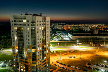 Fototapeta na wymiar Night panorama of the city. Tall apartment buildings illuminated by night illumination. Top view of windows and roofs of houses