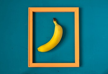Minimalistic still life in the style of pop art food. A modern creative concept of a fruit diet. Banana in a wooden frame on a sea-green surface. View from above.