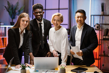 Portrait of creative multiethnic business team standing together at the table with gadgets and...