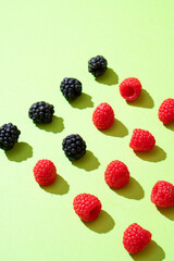 Raspberries and blackberries on a green background are evenly laid out. hard sunlight