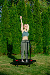 girl does Jumping fitness on trampoline in outdoor on green grass and trees on background