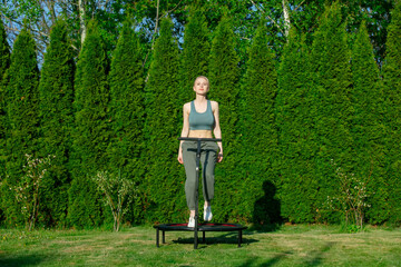 Fototapeta premium girl does Jumping fitness on trampoline in outdoor on green grass and trees on background