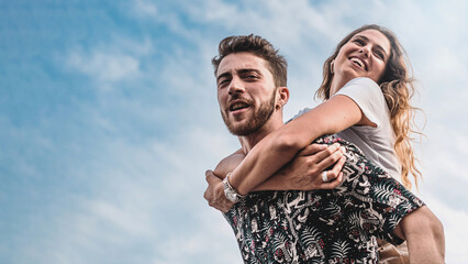 Couple of young people carefree piggybacking against the sky in the summer - life style concept of...