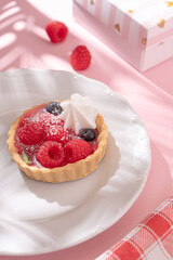 Tartlet with fresh berries in jelly and with meringue on a pink table