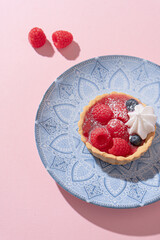 Tartlet with fresh berries in jelly and with meringue on a pink table