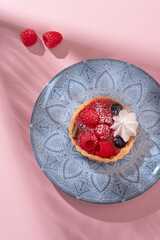 Tartlet with fresh berries in jelly and with meringue on a pink table