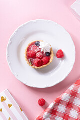 Sandless cake with cream and blueberries, and raspberry on a white plate on a pink table
