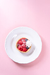Sandless cake with cream and blueberries, and raspberry on a white plate on a pink table