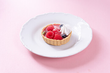 Sandless cake with cream and blueberries, and raspberry on a white plate on a pink table