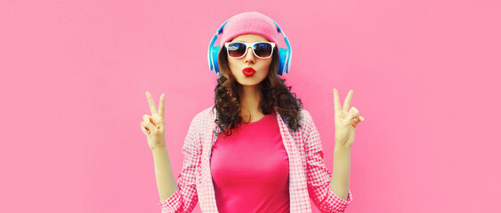 Summer colorful portrait of stylish modern young woman listening to music in headphones posing on pink background