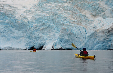 Two kayaks in the rain approaching deep blue glacier