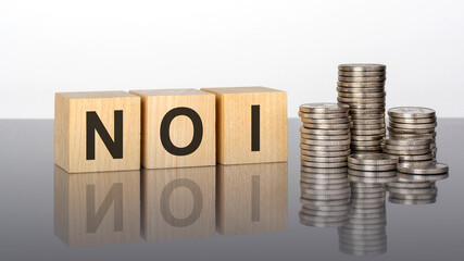 noi - text on wooden cubes on a cold grey light background with stacks coins