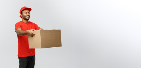 Delivery Concept - Portrait of Happy African American delivery man in red cloth holding a box...