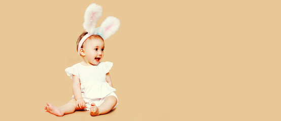 Portrait of cute baby with rabbit ears sitting on brown background