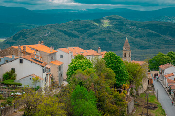 Obraz premium Panoramic view from the hill of Motovun city looking down towards the Mirna river on a cloudy sčring day. Red roofs and church in the foreground.