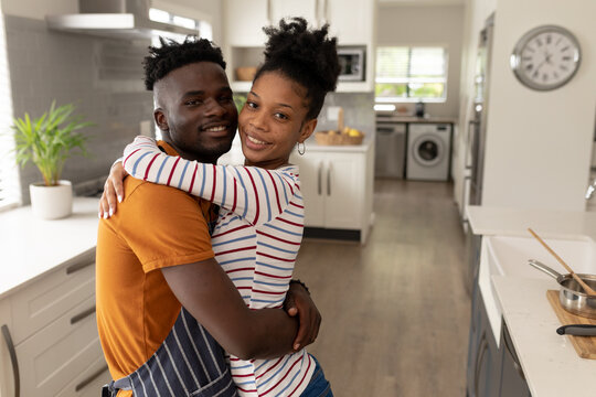 Portrait of smiling african american young boyfriend embracing girlfriend while standing in kitchen