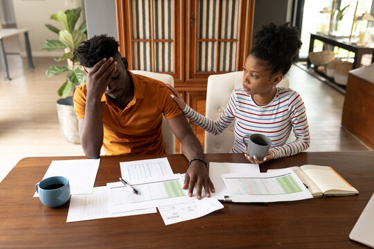 African american young woman with bills on table holding mug consoling stressed boyfriend at home