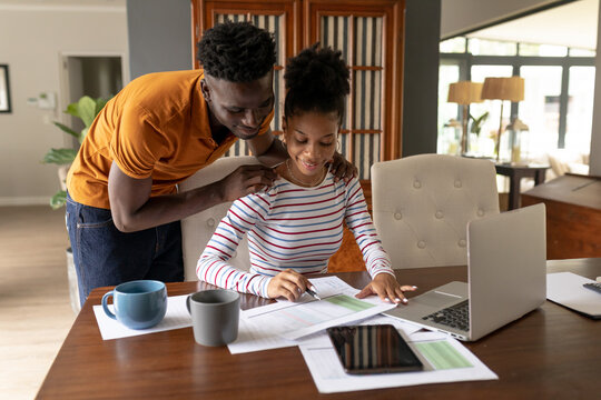 African american young man assisting girlfriend analyzing bills by laptop on table at home