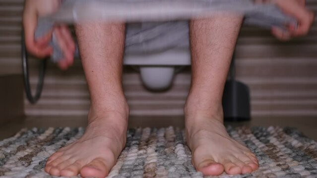 Man sitting in toilet. Diarrhea concept. Hairy legs of a man with grey underwear pantys moving feet.