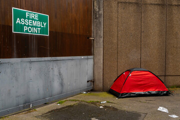 Simple red tent on a sidewalk of a street in a city. Homeless life in town. Social and poverty problem. Living in poverty. © mark_gusev