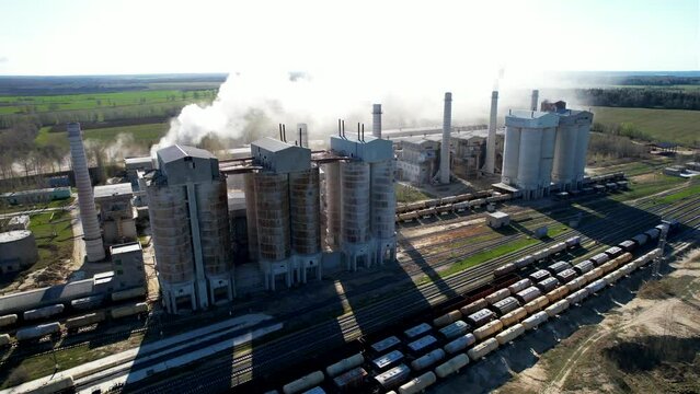 Smoke from pipes of cement plant. Сement Factory with smoke pipe. Chimney smokestack emission. Cement freight cars on railway. Transport bulk materials on railroad. Tank cars near industrial plant.
