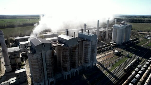 Smoke from pipes of cement plant. Сement Factory with smoke pipe. Chimney smokestack emission. Cement freight cars on railway. Transport bulk materials on railroad. Tank cars near industrial plant.
