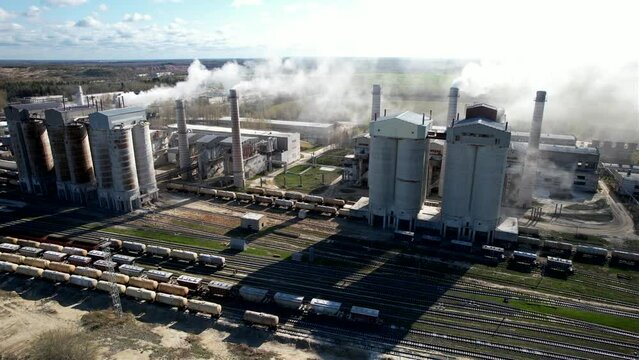 Smoke from pipes of cement plant. Сement Factory with smoke pipe. Chimney smokestack emission. Cement freight cars on railway. Transport bulk materials on railroad. Tank cars near industrial plant.
