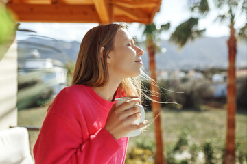 Fototapeta premium Young woman enjoying the view from apartment,drinking morning coffee on the balcony.