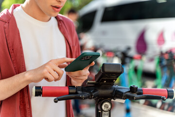 Fototapeta na wymiar Man using smartphone to unlocking urban kick scooter during the warm summer day