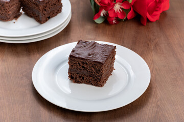 slice of chocolate cake covered with chocolate, served chilled, a bouquet of red roses next to the plate