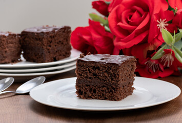 slice of chocolate cake covered with chocolate, served chilled, a bouquet of red roses next to the plate
