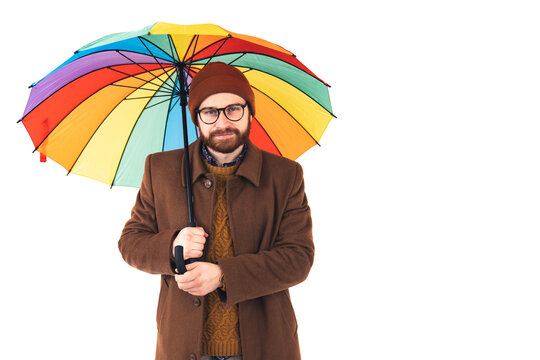 Studio shot on white background of a confident unshaved handsome caucasian man wearing autumnal outfit holding a colorful rainbow umbrella. High quality photo
