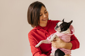 Attractive young caucasian girl looks at pet holding in arms on white background. Dog and its owner...